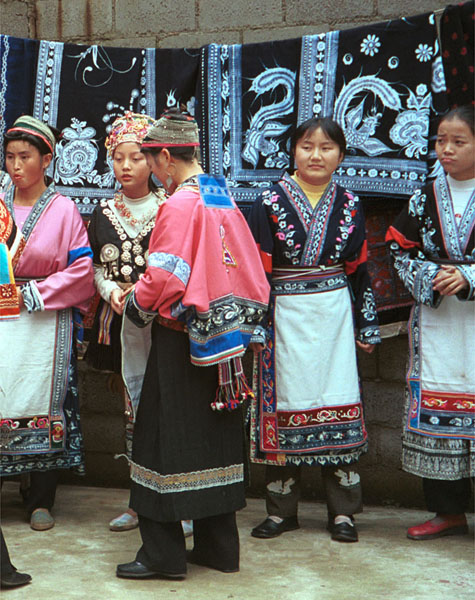 Jpeg 116K Group of Miao women wearing a mixture of clothing including wax resist (batik) and embroidery. The traditional costume has absorbed styles from other Miao as well as other influences. Note the traditional festival hair styles of some of the women. Lou Jia Zhuang village, Anshun city, Guizhou province 0110B12a