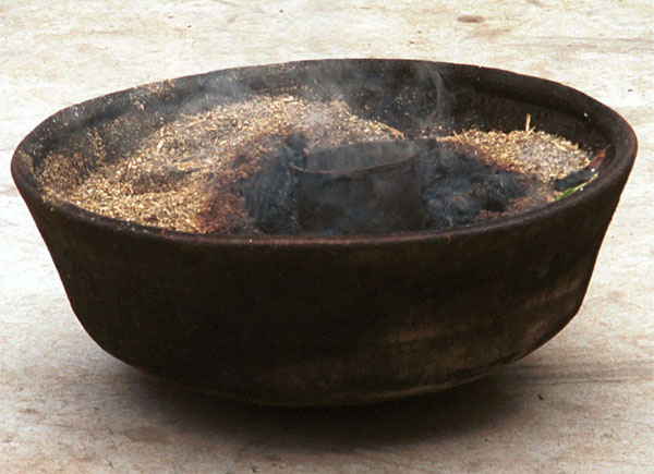 Jpeg 66K The wax pot heating in a bowl of burning material. The wax heats more steadily and maintains the optimum heat to keep the wax at the correct consistency rather than being on direct flame which overheats the wax. Lou Jia Zhuang village, Anshun city, Guizhou province. 0110B16