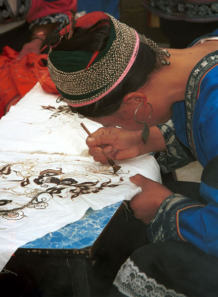 Jpeg 73K Miao woman wearing festival costume and hair style using her la dio (literally 'wax knife') to apply the wax resist la ran (literally 'wax dye') in a floral style. Lou Jia Zhuang village, Anshun city, Guizhou province 0110B19