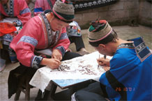 to Jpeg 81K Two Miao women wearing their festival costumesworking on wax resist (batik) in the floral style which may the reason for their nickname 'Flower Miao'. Note the front and back of their traditional hair styles. Lou Jia Zhuang village, Anshun city, Guizhou province 0110B24