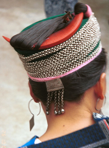 Jpeg 65K Miao woman showing her traditional hair style (and three la dio (wax knives) tucked into her hair near the right point of her circular comb. Cotton thread and strips of fabric have been used to help secure the coils of hair around the head before the chains are wrapped around. Lou Jia Zhuang village, Anshun city, Guizhou province 0110B27