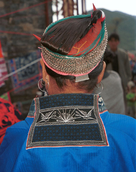 Jpeg 84K Miao woman showing her traditional hair style. A circular hair comb is used with cotton thread and strips of fabric to help secure the coils of hair around the head before the chains are wrapped around. Note the machine embroidered butterflies on the back of the neck of her jacket. Lou Jia Zhuang village, Anshun city, Guizhou province 0110B35