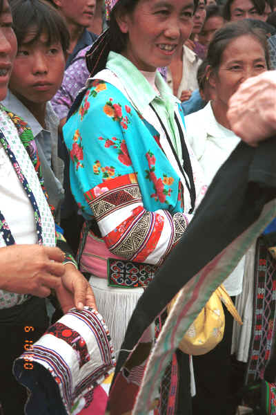 White Miao women standing with appliqued head pieces and showing fine applique (reverse applique) on jacket armbands - a style which is used on both head pieces, waist ties and jacket armbands - Ma Wo village, Zhe Lang township, Longlin county, Guangxi province 0010j27.jpg