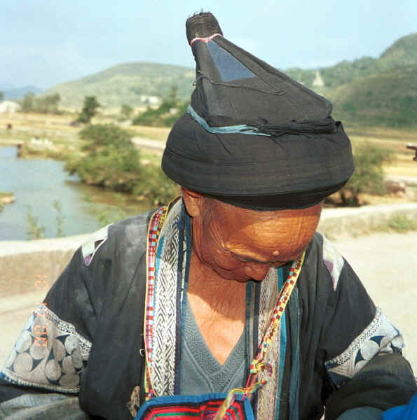 Old Bouyei textile seller getting ready to model the jacket which I had just bought and making sure she is properly dressed for a photo - Shitou village, Huanggousu township, Zhen Nin county, Guizhou province 0010u08.jpg