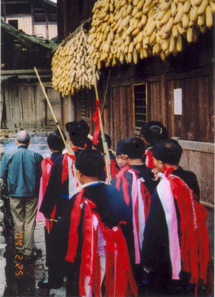 Jpeg 57K e27e 25 February 2004, the fourth day of the festival, in Langde village, Guizhou province, On this day, the ceremony was to take the spirit of the mountain dragon inside each home to live there so the family would enjoy good fortune in the future. The shaman and a group of men all wore traditional dress. These men were the leading people of the ceremony and of the community. They must be well thought of by the villagers before they can be selected as participants or else they cannot play the roles. When the ceremony started, the shaman went in front leading the way to each home. On entering each family's house they were offered cups of rice wine by the head of the family and fire crackers were also set off. While in the house, they played lusheng and danced in a circle to the rhythm of the bronze drum. When leaving the house, the owner gave them some red ribbons and cigarettes.