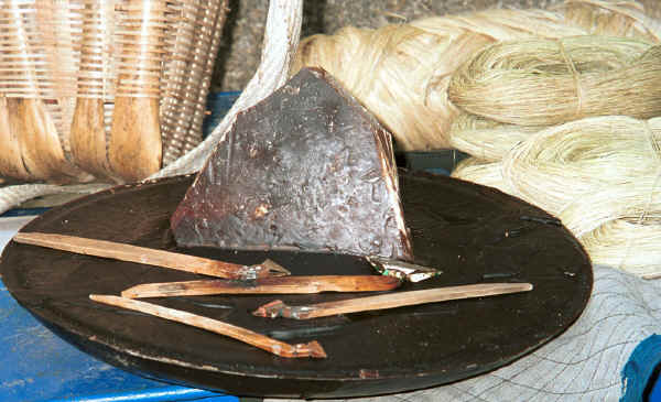 Big Flower Miao - block of wax with instruments for batik in foreground.  To the right the small balls of fibre are spliced hemp.  the larger bundle of wound fibre behind is ramie which has been stripped from the branch but not yet spliced.  Note that the the hemp (especially where it has not been lightened by the flash bulb) is a darker colour than the ramie.  Xian Ma village, Hou Chang township, Puding county, Guizhou province 0010y10.jpg