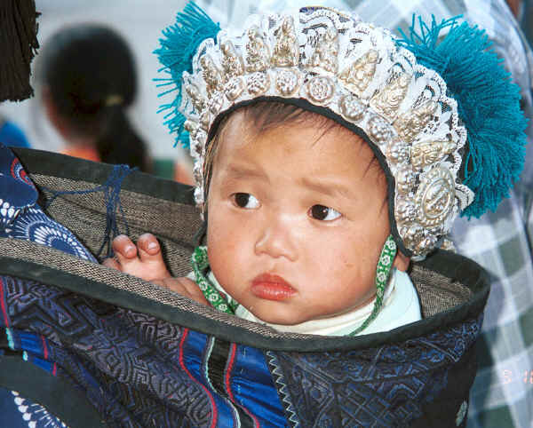 Black Miao baby showing hat adorned with white metal budhas in an embroidered baby carrier lined with hand woven cloth, Zuo Qi village, Min Gu township, Zhenfeng county, Guizhou province 0010q33.jpg