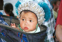 Jpeg 45K Black Miao baby showing hat adorned with white metal budhas in an embroidered baby carrier lined with hand woven cloth, Zuo Qi village, Min Gu township, Zhenfeng county, Guizhou province 0010q33.jpg