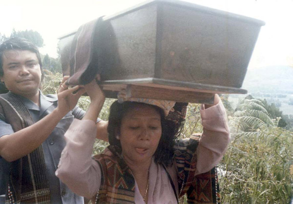 Close up of Oloan carrying the casket and wearing the sadum woven by her mother and assisted by Simon, the eldest male descendent of Jakobus and Nai Horja (and brother of Vera). He has a ragi hotung over his shoulder and there is a folded one lying over the casket. These are similar to the ones shown in the Vera Tobing collection.