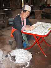 to Jpeg 59K White Hmong woman in Ban Pha-nok-kok village waxing cloth before dyeing. Note the wax heating in hot ashes  3439