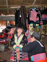 to Young White Hmong girl in Ban Pha-nok-kok village being dressing in traditional festival clothing by her mother and grandmother