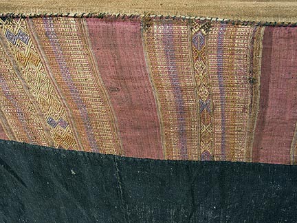 Jpeg 66K Detail of supplementary weft top band of a Tai Daeng Mosquito Net (pha mung) from Xam Tai in northeast Laos. Approximately: 61" x 65" on the sides and 60" high; hanging pockets extends 4" from main 'box'. Four panels on each side of handspun, handwoven indigo cotton, with silk and cotton heading border in good condition; top of four panels (one is pieced making three parts) gold-colored handspun, handwoven cotton. One side (side 'd') has a panel replaced, or of darker color indigo. Several patches and some holes, although none are larger than 1". A few patches of supplementary warp scraps. All handstitched. Early 20th century.