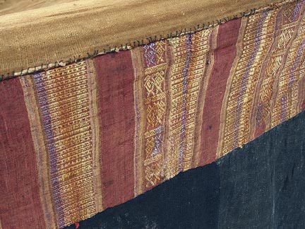 Jpeg 71K Detail of supplementary weft top band of a Tai Daeng Mosquito Net (pha mung) from Xam Tai in northeast Laos. Approximately: 61" x 65" on the sides and 60" high; hanging pockets extends 4" from main 'box'. Four panels on each side of handspun, handwoven indigo cotton, with silk and cotton heading border in good condition; top of four panels (one is pieced making three parts) gold-colored handspun, handwoven cotton. One side (side 'd') has a panel replaced, or of darker color indigo. Several patches and some holes, although none are larger than 1". A few patches of supplementary warp scraps. All handstitched. Early 20th century.