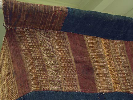 60K Jpeg Top corner detail of Tai Daeng Mosquito Net (pha mung) from Xam Tai in northeast Laos. Approximately: 61" x 65" on the sides and 60" high; hanging pockets extends 4" from main 'box'. Four panels on each side of handspun, handwoven indigo cotton, with silk and cotton heading border in good condition; top of four panels (one is pieced making three parts) gold-colored handspun, handwoven cotton. One side (side 'd') has a panel replaced, or of darker color indigo. Several patches and some holes, although none are larger than 1". A few patches of supplementary warp scraps. All handstitched. Early 20th century.