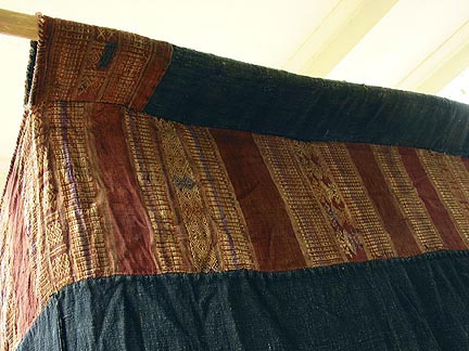 Jpeg 54K Top corner detail of Tai Daeng Mosquito Net (pha mung) from Xam Tai in northeast Laos. Approximately: 61" x 65" on the sides and 60" high; hanging pockets extends 4" from main 'box'. Four panels on each side of handspun, handwoven indigo cotton, with silk and cotton heading border in good condition; top of four panels (one is pieced making three parts) gold-colored handspun, handwoven cotton. One side (side 'd') has a panel replaced, or of darker color indigo. Several patches and some holes, although none are larger than 1". A few patches of supplementary warp scraps. All handstitched. Early 20th century.