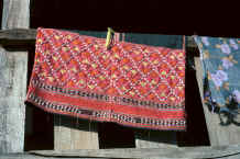 to Jpeg 31K A Sgaw Karen traditional woman's blouse hanging out to dry showing at the bottom the koh dyed (red) cotton embroidery and added Jacob's seeds on the indigo dyed, hand woven base 8812o35B.jpg