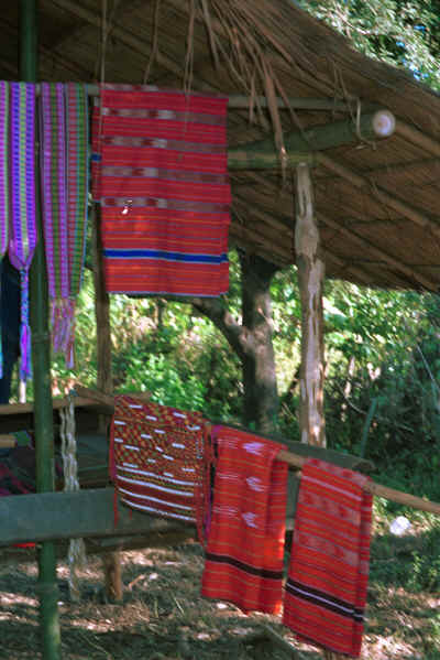 Hand woven koh (red) dyed handwoven sarongs with ikat dyed stripes hanging with a hand woven blouse and bands 8812p02.jpg