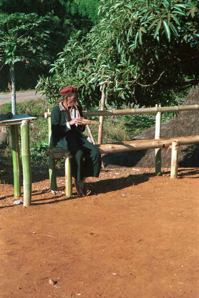 U Lo-Akha man playing a musical gourd and bamboo pipes for young boys to sing a welcome at the entrance to a village in the hills around Chiang Rai 8812p12.jpg