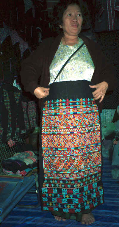 A Yao woman in the Chiang Mai night market holding up a trouser panel for a pair of women's trousers which she had embroidered and which is now in my textile collection 8812m13.jpg