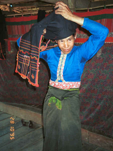 Jpeg 33K Black Thai lady showing how her head cloth is worn.  Note the curtains behind shielding off the sleeping areas from view and with hand woven cloth pieced into the heading area of the curtains.  Dien Bien Phu, Lai Chau Province 9510D23.JPG