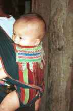 to Jpeg 34K Black Thai baby in a baby carrier made with an insertion of supplementary woven cloth and layers of edging made from individually folded 'points'.  A village near Dien Bien Phu, Lai Chau Province. 9510E22.JPG