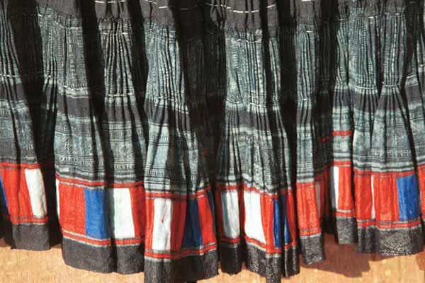 Jpeg 39 K  9510G20 Close up of part of a Flowery Hmong woman's short pleated skirt hanging out to dry outside a house in small road-side village near Phong Tho (Phong Thanh) in Lai Chau Province. The skirt is dyed a dark indigo after very many dippings in the dye vat.  Note the inserted strip of wax resist fabric and the strip of pieced red, blue and white fabric squares from purchased fabric