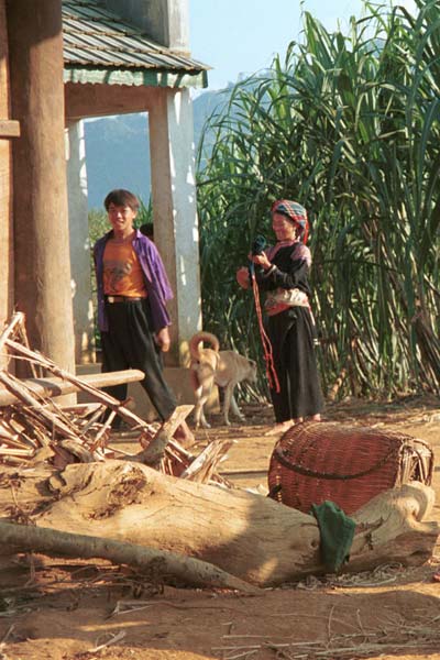 Jpeg 53K 9510G23 Young Flowery Hmong male with an older Flowery Hmong woman.  It appears that she is not wearing a short batik skirt but a longer indigo dyed wrap around one.  Outside a house in small road-side village near Phong Tho (Phong Thanh) in Lai Chau Province.