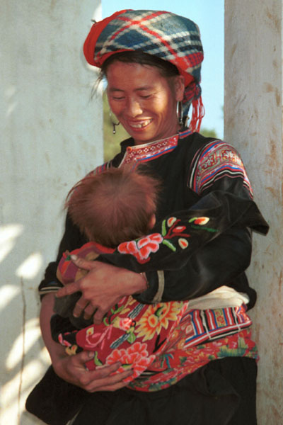 Jpeg 53K 9510G27  Flowery Hmong mother with her baby outside a house in small road-side village near Phong Tho (Phong Thanh) in Lai Chau Province.